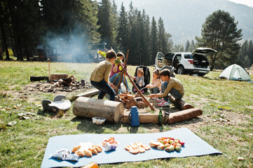 Family bonfire in mountain. Frying sausages. Mother with four kids camping. Autumn hike and camp weather. Warming and cooking near flame together.