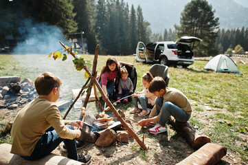 Family bonfire in mountain. Frying sausages. Mother with four kids camping. Autumn hike and camp...