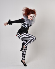 Full length  portrait of red haired  girl wearing a black and white clown jester costume, theatrical circus character.  Standing pose  isolated on  studio background.