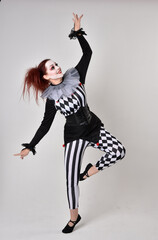 Full length  portrait of red haired  girl wearing a black and white clown jester costume,...