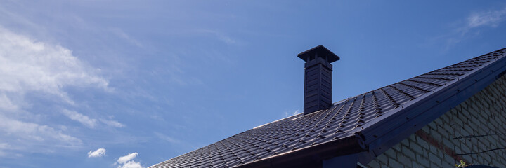 metal roof on the roof of the house with a pipe against the blue sky