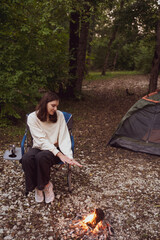 Woman sitting by the fire in the woods. Enjoy a picnic in nature