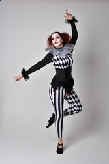 Full length  portrait of red haired  girl wearing a black and white clown jester costume, theatrical circus character.  Standing pose  isolated on  studio background.