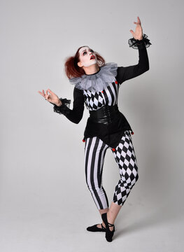 Full length  portrait of red haired  girl wearing a black and white clown jester costume, theatrical circus character.  Standing pose  isolated on  studio background.