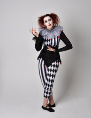 Full length  portrait of red haired  girl wearing a black and white clown jester costume,...
