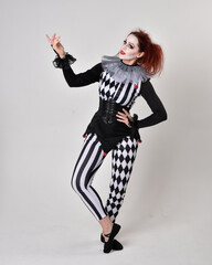 Full length  portrait of red haired  girl wearing a black and white clown jester costume,...
