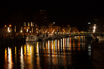 Klaipeda, Lithuania - 11 28 2020: boats at night. Beautiful city lights illumination reflecting in the water, boats and buildings, calm November street. A night city photo good for touristic booklets
