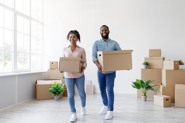 Fototapeta na wymiar Cheerful millennial african american couple carry cardboard boxes with things in room interior