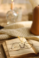 Butternut squash, soft blanket, open book, reading glasses and lit candles. Autumn season, hygge at home. Selective focus.