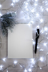 a notebook in a Christmas garland with a branch of a fir tree in silver color, a black pen. light background