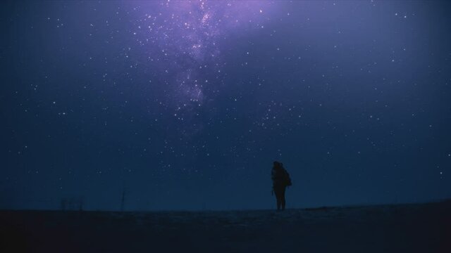 Woman standing alone in the field at night, looking up to the milky way galaxy full of stars on a starry night sky. Tracking shot. 