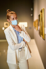 Fototapeta na wymiar Woman visitor wearing an antivirus mask in museum looking at pictures.