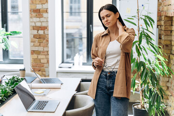 Neck ache concept. Young woman standing at office and feeling hurt having pain in her neck. Woman...