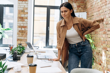 Full length view of the sad caucasian woman have a backache in her office because sitting all day....
