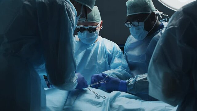 Multiracial team of professional medical surgeons performs the surgical operation in a modern hospital. Doctors are working to save the patient. Medicine, health, cardiology and transplantation.