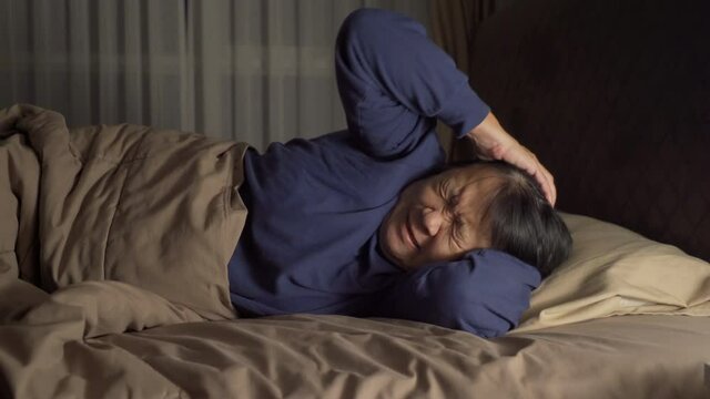 Unhappy elderly old Asian woman, person is terrified from disturbing nightmare, sleeping with stress on bed in bedroom at home. Insomnia.