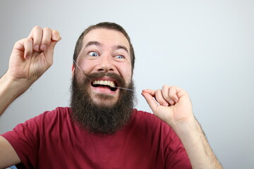 Young bearded man removes bacteria, plaque and food from between teeth. Using dental floss. 