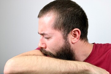 Sick caucasian man sneezing into elbow