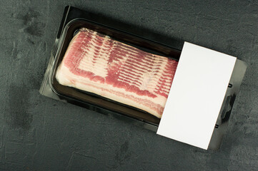 smoked pork bacon in factory plastic packaging on a black background. top view. logo layout design.