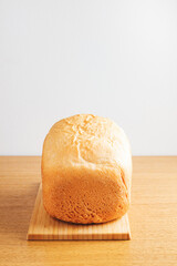 Homemade white wheat bread with golden crust on wooden cutting board and wooden table against white wall.