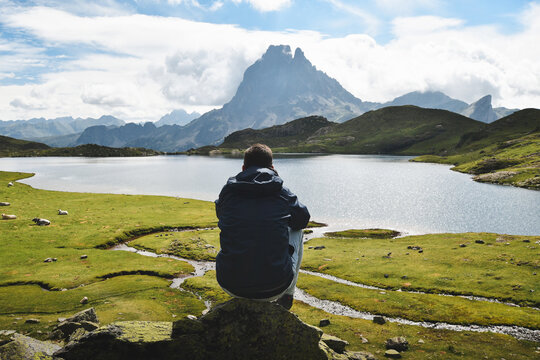 Hiker sitting on a rock and looking at great panoramic view of Lac Gentau, Lacs d'Ayous, Parc national des Pyrenees, France
