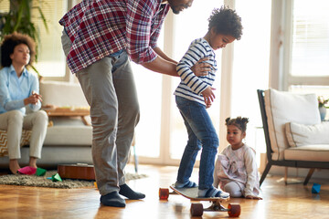 A young father teaches his son riding the skateboard at home. Family, together, love, playtime