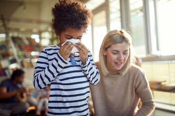 A cute little boy blows his nose into a tissue while spending quality time with his mother at home. Family, home, together