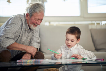 A little grandson enjoys drawing while spending a quality time with his grandpa at home. Family, home, playtime