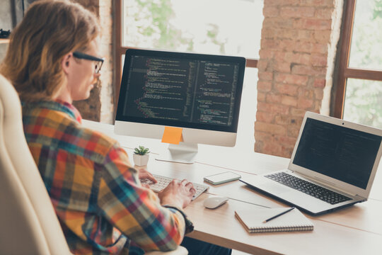 Back rear view photo of young man use laptop programmer coder jawascript linux developer sit desk indoors