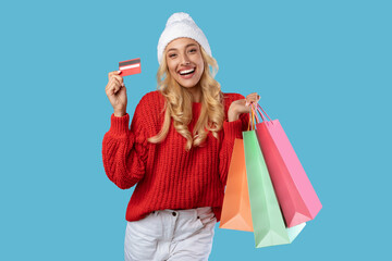 Happy woman holding credit card carrying shopping bags in winter