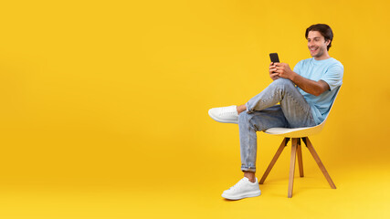 Happy guy using cellphone at studio, sitting on chair, banner