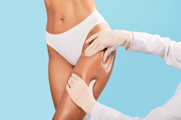 Woman having lipolysis treatment at beauty salon, doctor examining thigh