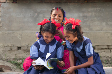 Village woman braiding the hair of her school going daughter sitting on a cot in their house