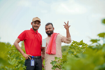 Indian farmer showing smartphone with agronomist or officer at agriculture field.