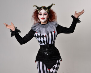 close up portrait of red haired  girl wearing a black and white clown jester costume, theatrical circus character.  Standing pose  isolated on  studio background. - obrazy, fototapety, plakaty