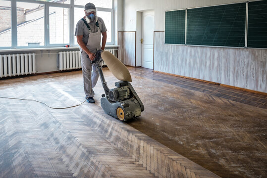 Worker polishing hardwood parquet floor with grinding machine.