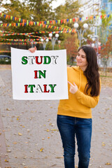 A woman smiles and holds a poster with the text Study in Italy