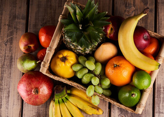 Mix of fresh juicy colorful exotic tropical fruits in basket on wooden background top view