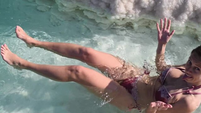 Slim woman in swimsuit bikini swim and lies in clear water of Dead Sea. Very salty water push out. Treatment and recreation in Israel, Dead Sea, salt and mud are good for health.