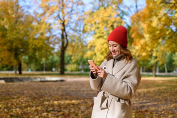 Woman reading messages or surfing internet from phone at autumn park