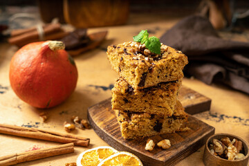 Pumpkin blondie bars with chocolate and walnuts close-up. Brownie pie slices on a serving wooden board on the dark culinary background. Baking for Thanksgiving