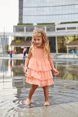 Naklejka premium happy baby girl play with water in a fountain on the square