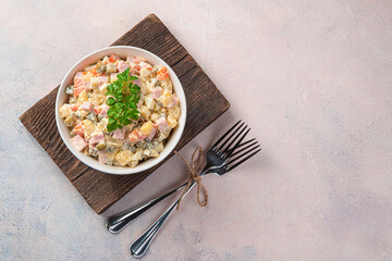 Classic olivier salad with fresh parsley on a light pink background. Top view, copy space.