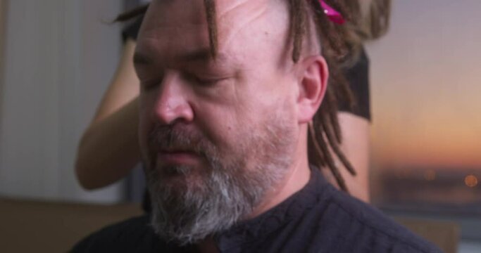 A master braids dreadlocks for a bearded man. Close-up. Long process.