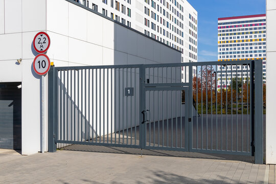 Entrance to the courtyard of a modern multi-storey residential complex. Lattice gates with a wicket and an entrance portal to the underground parking. Residents safety concept