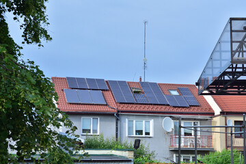 Solar panels on the roof of a small family house, trees and sky. Summer.