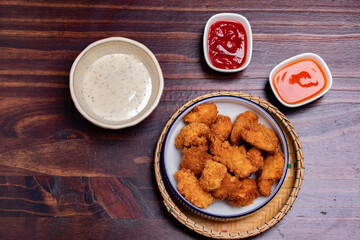 Fried chicken pops with ketchup, chili sauce and mayo on wooden background.