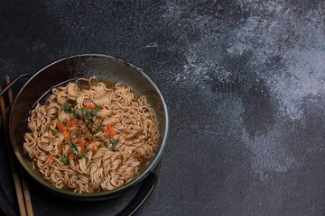 Instant noodles in gray Japanese ceramic lining with black tray, top view.
