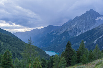 Landscape of Hochgall mountain peaks covered by clouds, valley and Antholzer See lake in Dolomites, Italy