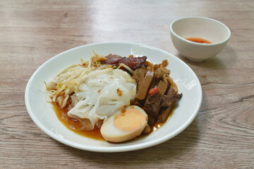 steamed large rice noodles topping slice fried Chinese sausage and pork belly with bean sprout dressing black soy sauce on plate dipping spicy chili sauce